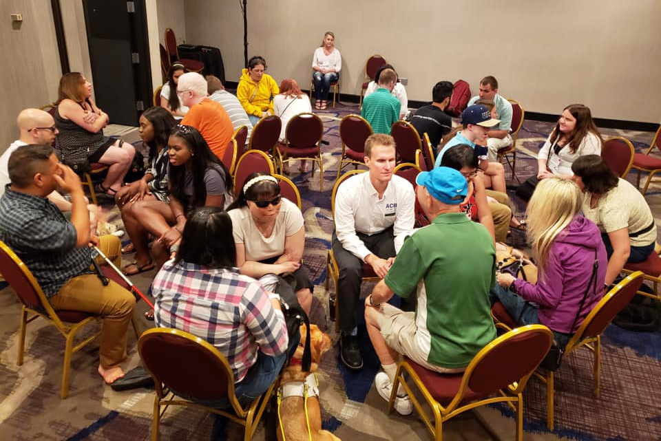 A group of blind and low-vision students gathered in a room participating in a lively breakout session